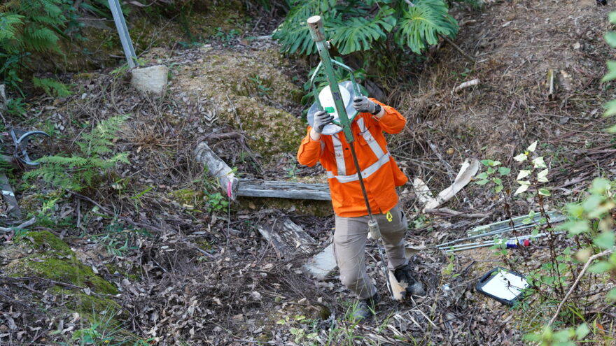 Person in high-vis jacket holding a pole, performing geotechnical testing.